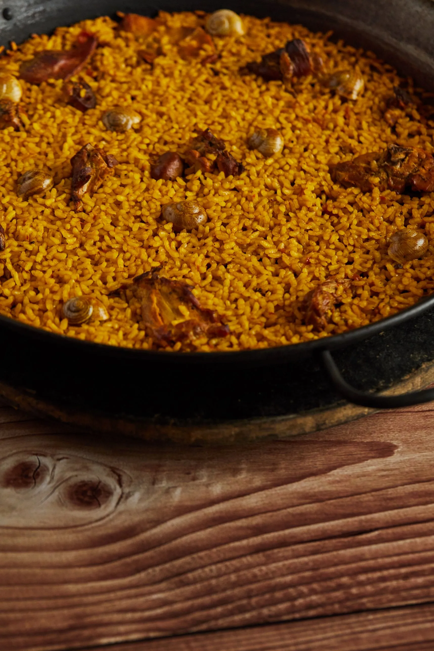 Rabbit and snail rice in an iron paella pan on a wooden table