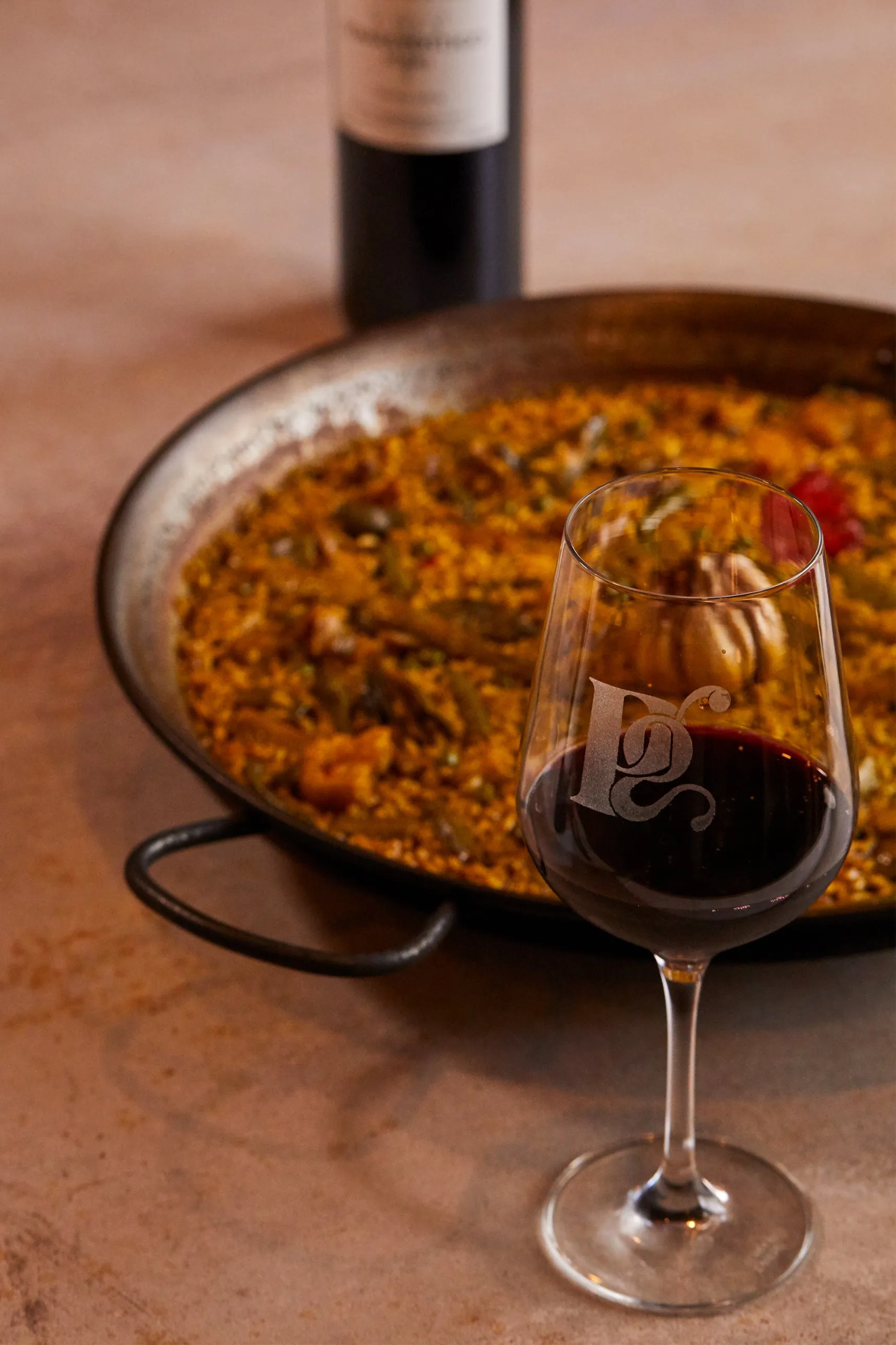Vegetable paella with a glass of red wine engraved with the Paco Gil logo