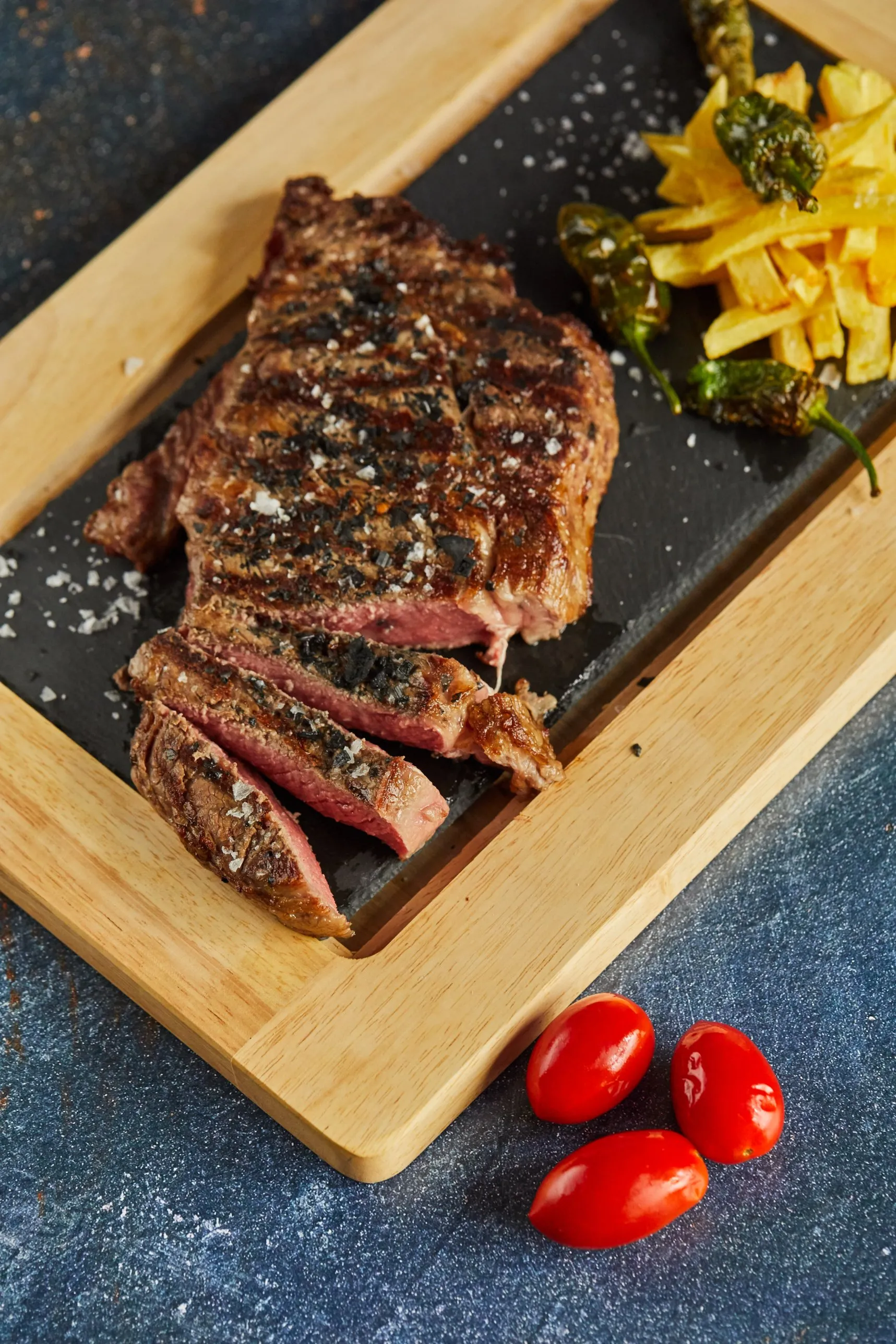 Chargrilled steak sliced on a slate board, with chips and Padrón peppers