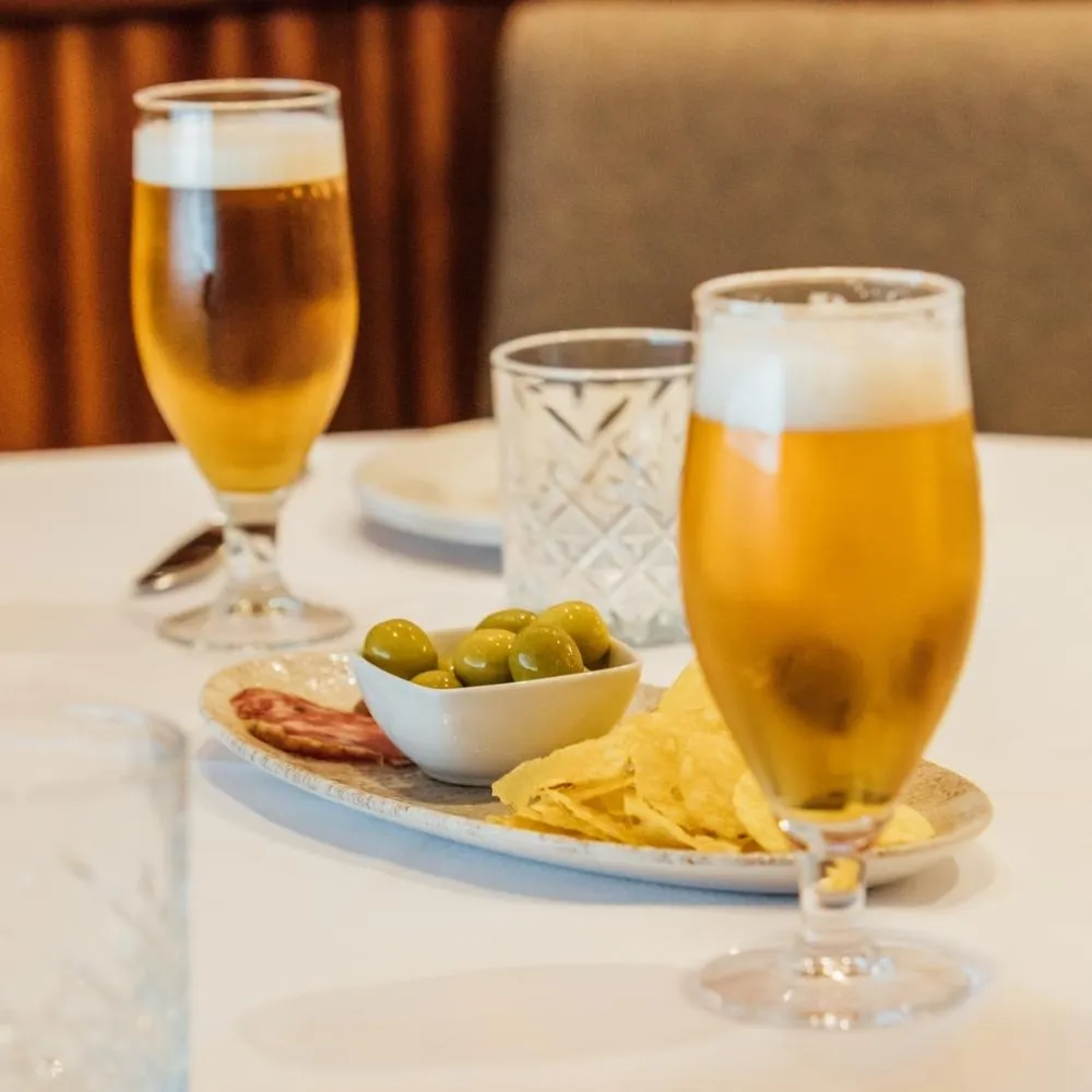 Two beers with olives, crisps and cured sausage