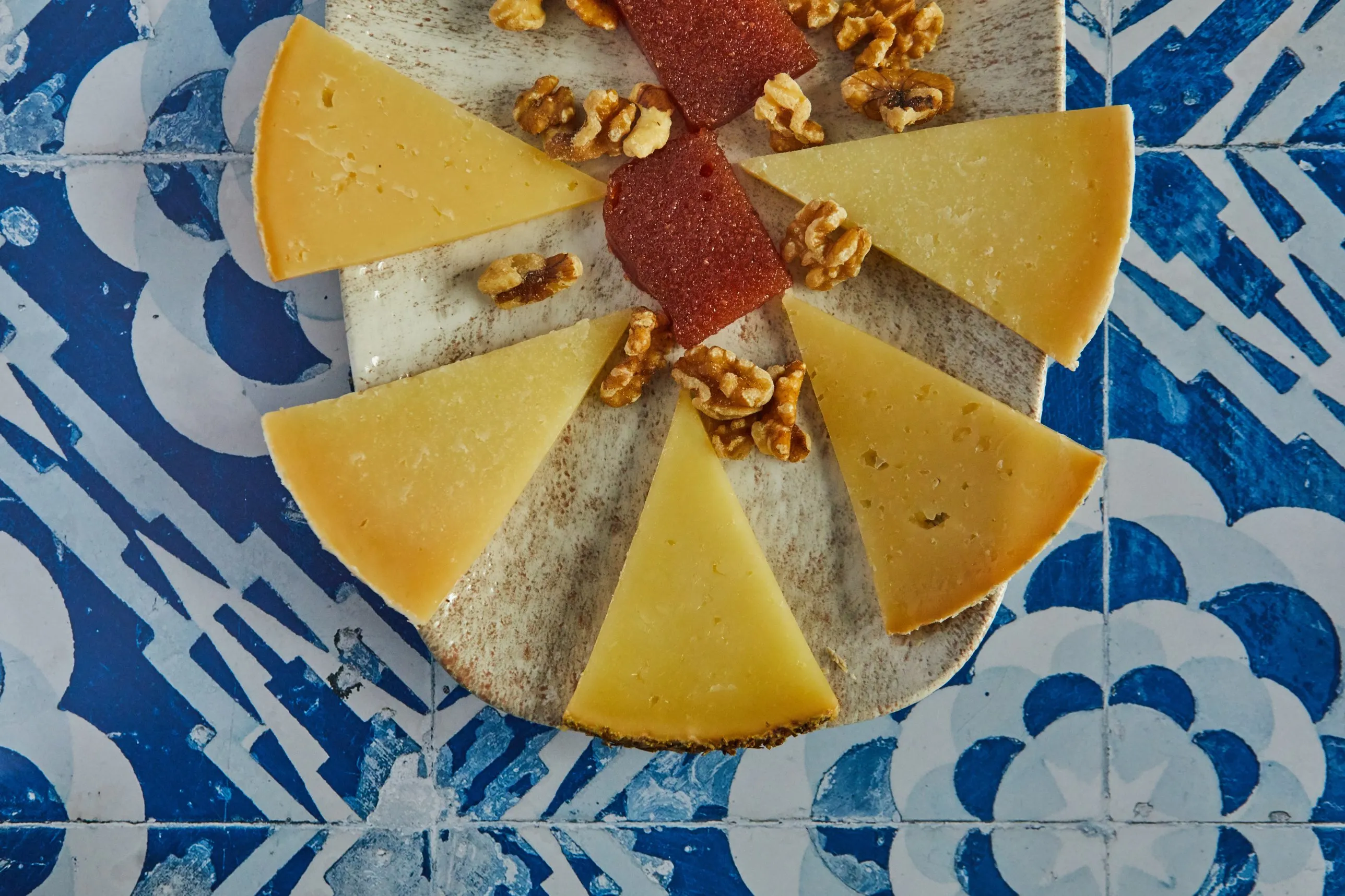 Cheese board with quince and walnuts on a tiled table