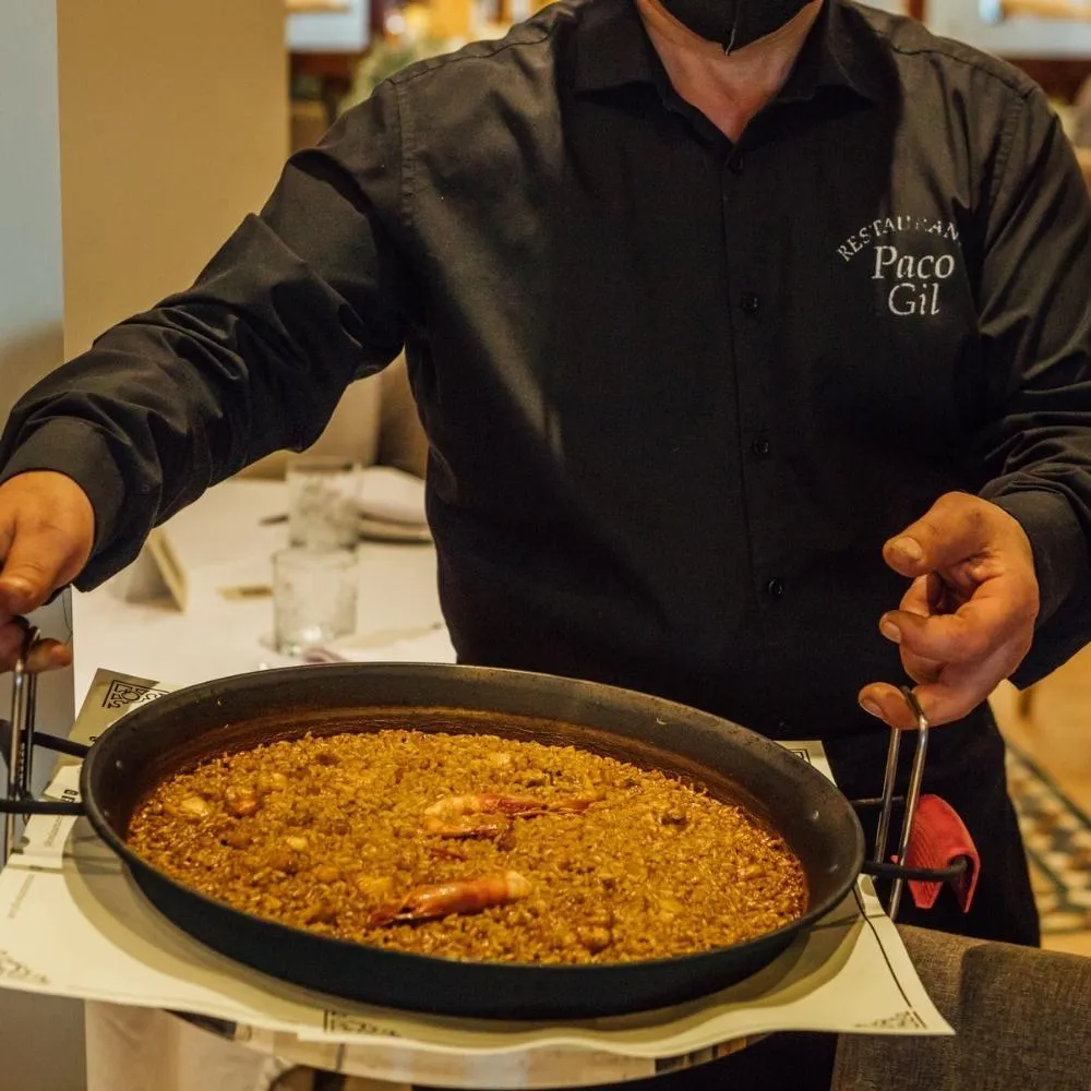 Waiter serving a freshly made rice dish in a paella pan